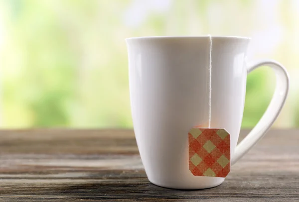 Bílý hrnek s sáček čaje na dřevěný stůl, zblízka — Stock fotografie