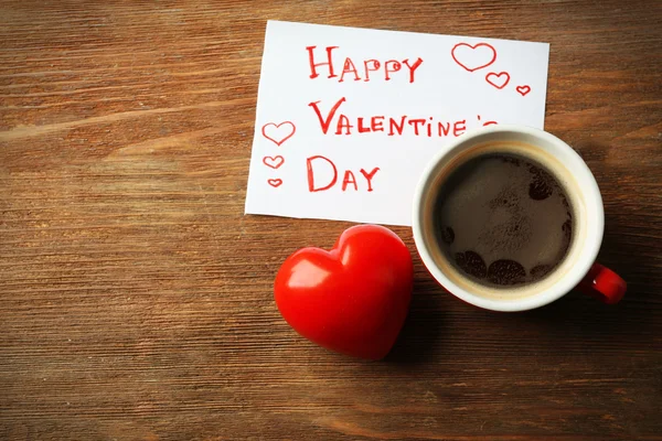 Valentine concept. Cup of coffee with red heart and note on wooden table background — Stock Photo, Image