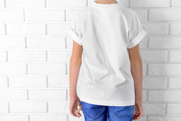 Publicidade de roupas. Menino em camiseta e jeans no fundo da parede de tijolo branco, close-up — Fotografia de Stock