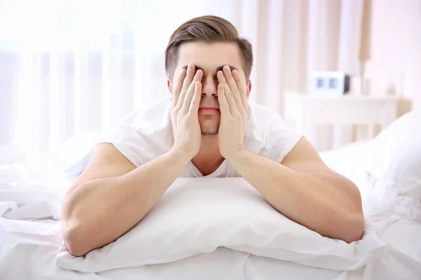 Young man closes eyes with hands in bed at home — Stock Photo, Image