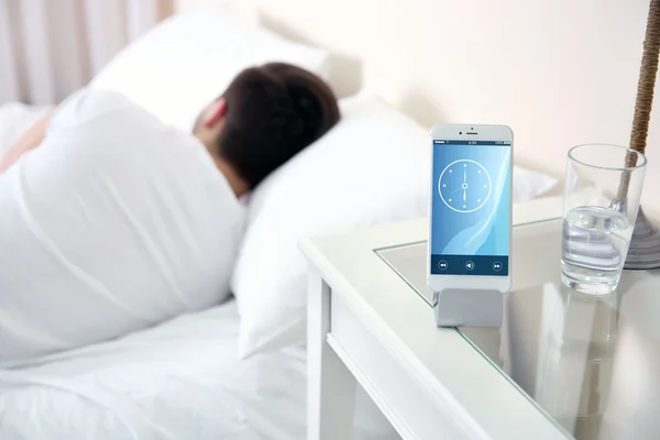 Jeune homme dormant dans le lit près de la table de chevet avec téléphone portable à la maison — Photo