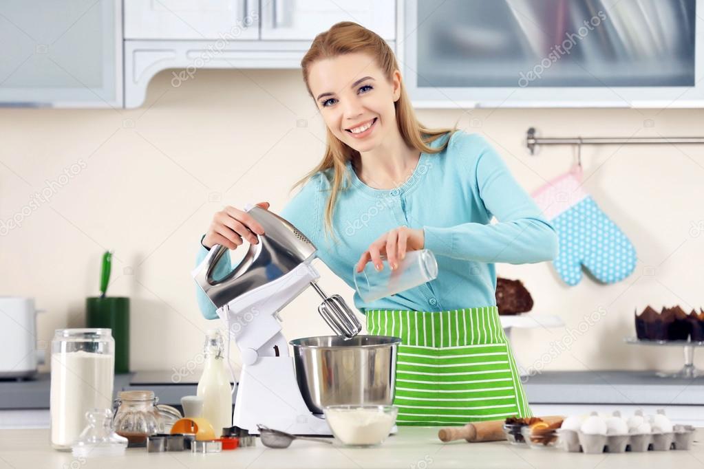 Young woman adding milk to a food processor to male a dough
