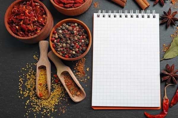 Especiarias sortidas com caderno de receitas em fundo de mesa preta — Fotografia de Stock