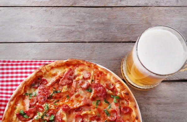 Gustosa pizza e bicchiere di birra sono sul tavolo di legno, da vicino — Foto Stock