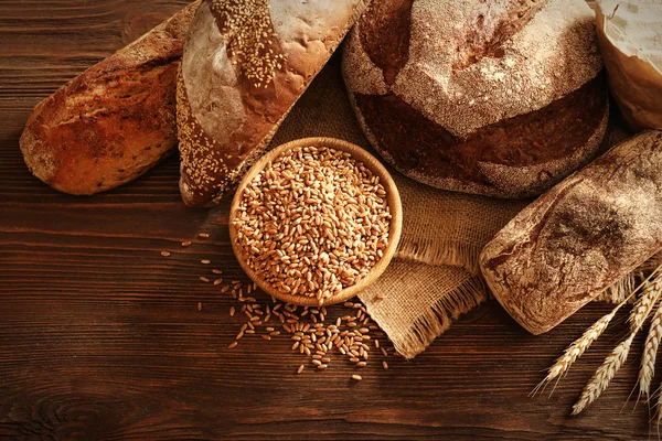 Свежий хлеб и миска пшеничных зерен на деревянном фоне — стоковое фото