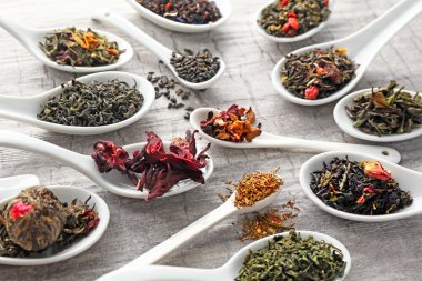 Gri ahşap arka plan üzerinde beyaz kaşık kuru çay çeşitli