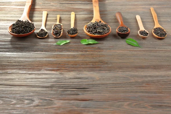 Trockener Tee mit grünen Blättern in Holzlöffeln auf Tischhintergrund, Kopierraum — Stockfoto