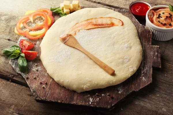 Свежее тесто, приготовленное для пиццы с помидорами и нарезанным перцем на деревянной доске, крупным планом — стоковое фото