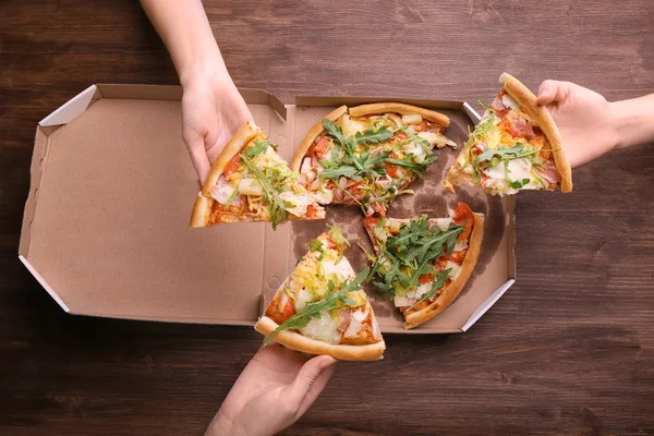 People hands with sliced pizza on wooden table closeup — Stock Photo, Image