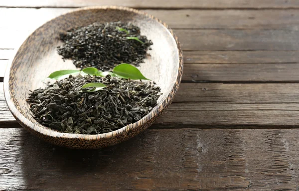 Tè secco in piatto con foglie verdi su sfondo tavolo di legno — Foto Stock