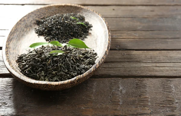 Dry tea in plate with green leaves on wooden table background — Stock Photo, Image