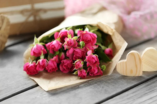 Rosas rosadas en una bolsa de papel y corazones decorativos en una mesa de madera, de cerca —  Fotos de Stock