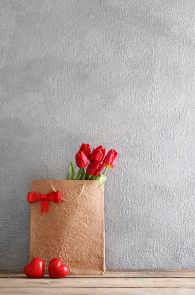 Tulipas vermelhas em saco de papel na mesa de madeira contra a parede cinza, close-up — Fotografia de Stock