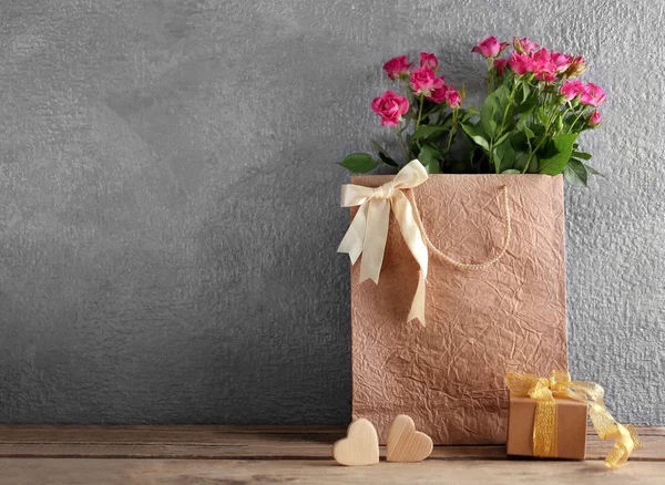 Pink roses in paper bag on wooden table against the grey wall, close up — Stock Photo, Image