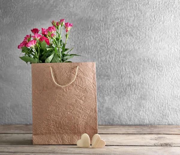 Розовые розы в бумажном пакете на деревянном столе против серой стены, закрыть — стоковое фото