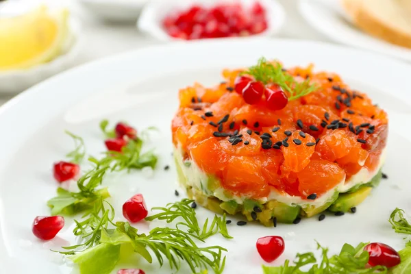 Fresh tartar with salmon, avocado, salad and black sesame on white plate, close up — Stock Photo, Image