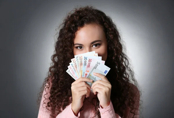 Beautiful young girl holding cash on grey background — Stock Photo, Image