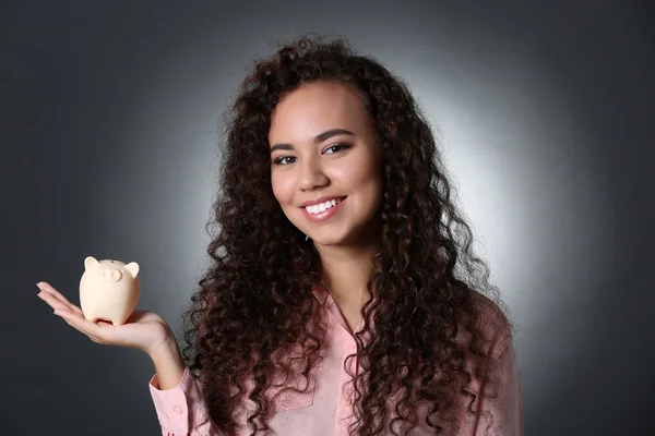 Menina bonita segurando banco porquinho no fundo cinza — Fotografia de Stock