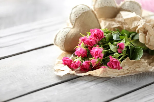 Ροζ τριαντάφυλλα σε ένα χαρτί και διακοσμητικό καρδιές σε έναν ξύλινο πίνακα, εσωτερικη — Φωτογραφία Αρχείου