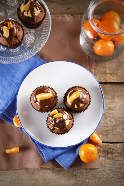 Three tasty cupcakes with slice of mandarin and chocolate on a plate over wooden background — Stock Photo, Image