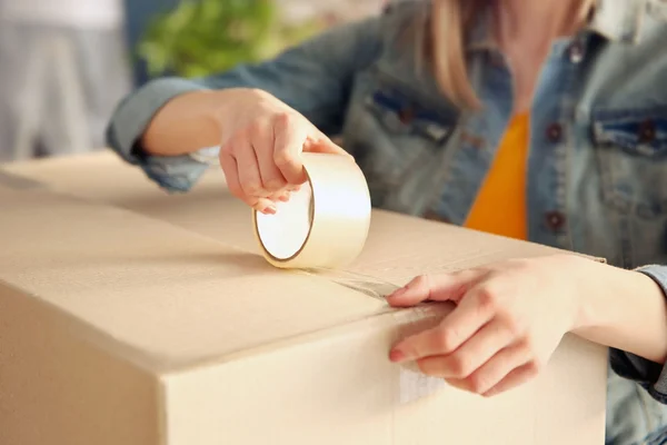 Young girl sealing with tape big cardboard box for moving