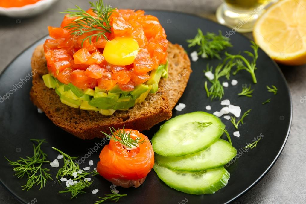 Frisches Tatar mit Lachs, Avocado, Eigelb und Schwarzbrot auf Teller ...