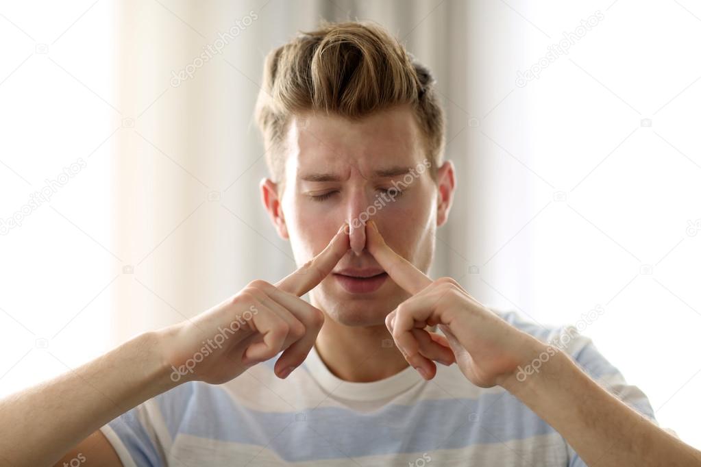 Young blonde man pinching his nose with two hands because of the stench in the room