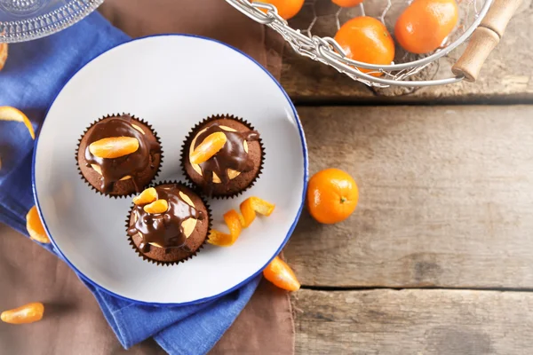 Tres sabrosos cupcakes con rebanada de mandarina y chocolate en un plato sobre fondo de madera —  Fotos de Stock