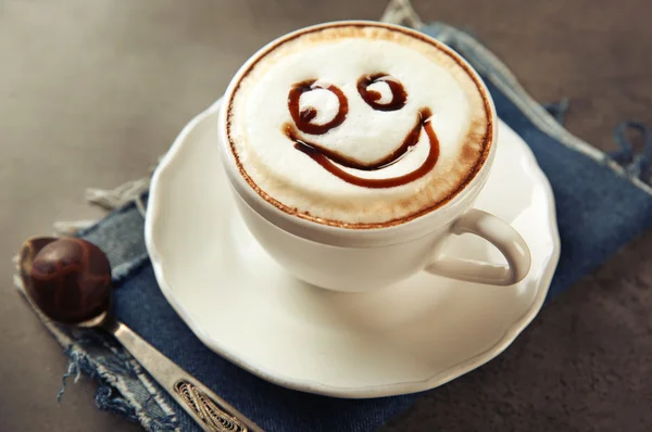 Tazza con cappuccino caldo con sciroppo di cioccolato e caramelle sulla tavola grigia — Foto Stock