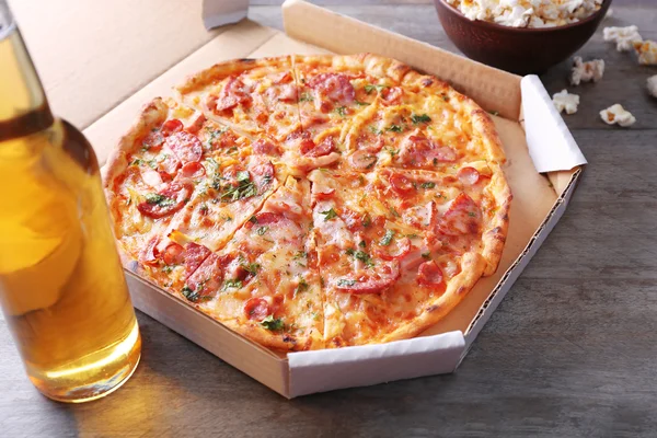 Lekkere pizza in karton en flesje bier zijn op houten tafel, close-up — Stockfoto