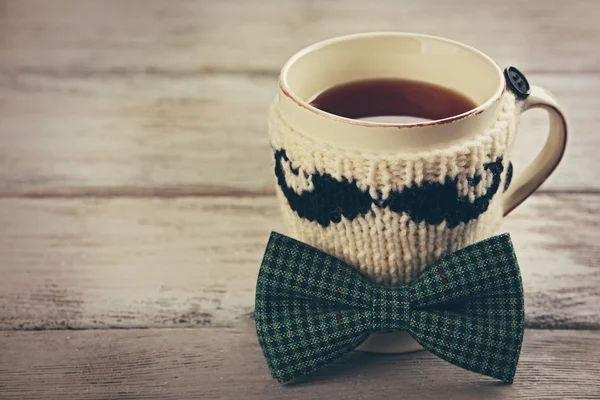 Pajarita y taza de té con bigote de punto sobre mesa de madera —  Fotos de Stock