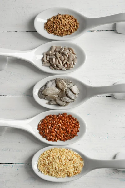 Různé druhy semen v lžíce na dřevěný stůl — Stock fotografie