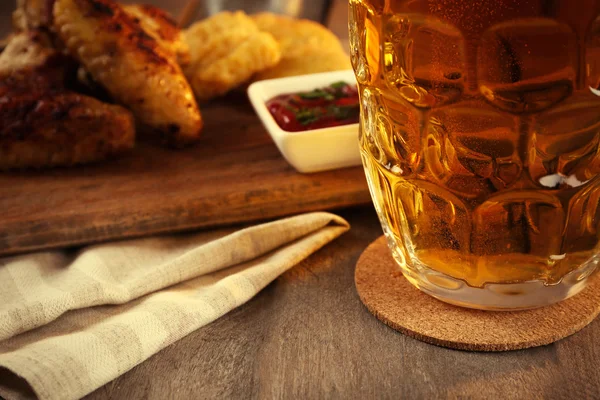 啤酒和鸡翅膀装在木桌上的玻璃关闭 — 图库照片
