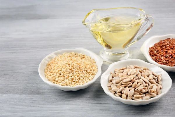 Different kinds of seeds with oil on wooden table — Stock Photo, Image