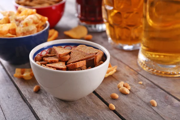 Mugs of beer and bowls with snacks on wooden table — Stock Photo, Image