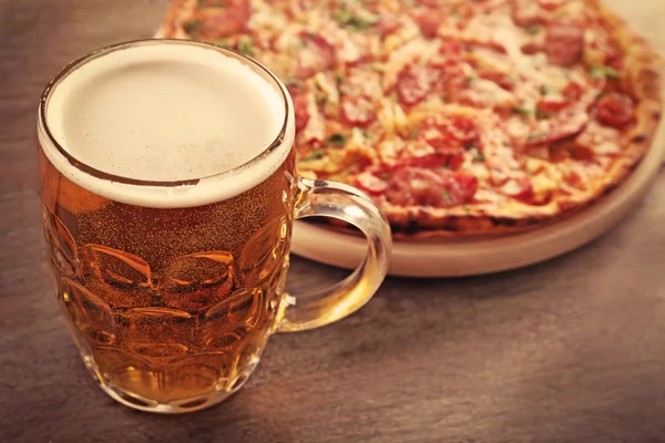 Sabrosa pizza y un vaso de cerveza están en la mesa de madera, de cerca — Foto de Stock