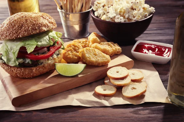 Großer leckerer Hamburger mit Snacks und Glasflasche Leichtbier auf Holztisch — Stockfoto