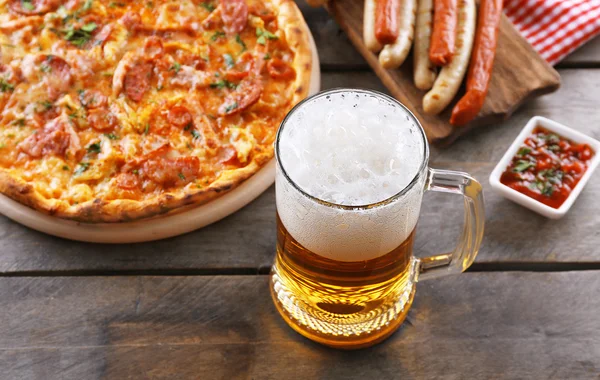 Embutidos a la parrilla, deliciosa pizza y vaso de cerveza sobre mesa de madera, de cerca — Foto de Stock
