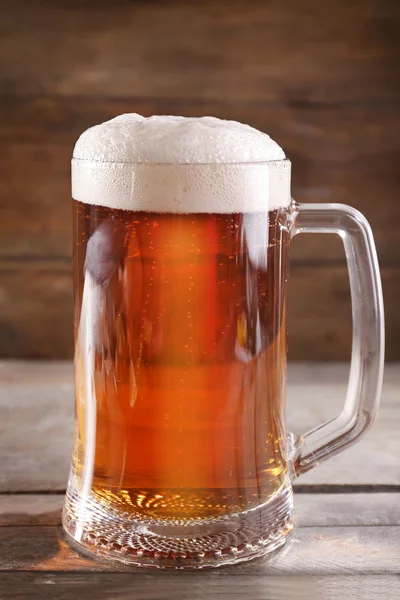 Glass mug of light beer on wooden table, close up