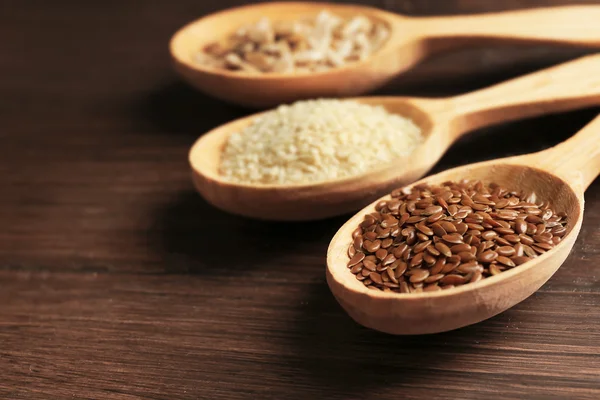 Sesame, flax and sunflower seeds in wooden spoons on table, closeup — Stock Photo, Image