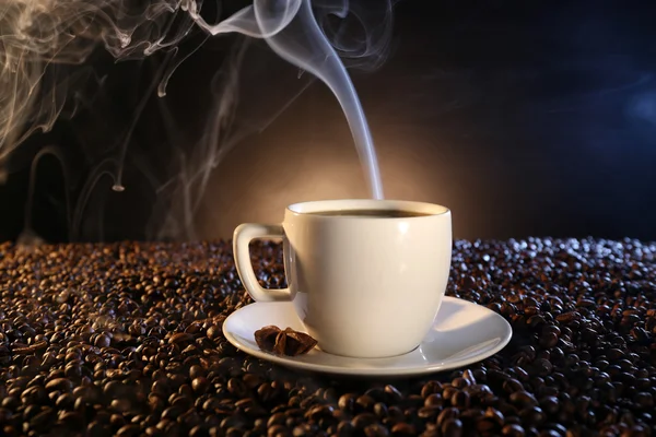 Cup of hot coffee among coffee beans on dark background Royalty Free Stock Images