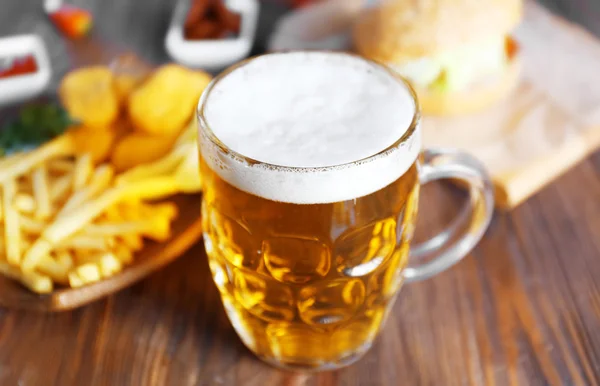 Glass mug of light beer with French fries on dark wooden table, close up — Stock Photo, Image