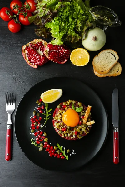 Beef tartare served in a round black plate on a dark desk, top view — Stock Photo, Image