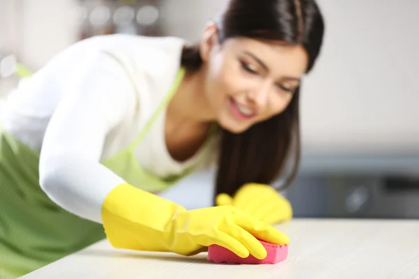 Bella donna in guanti protettivi pulizia tavolo da cucina con spugna — Foto Stock