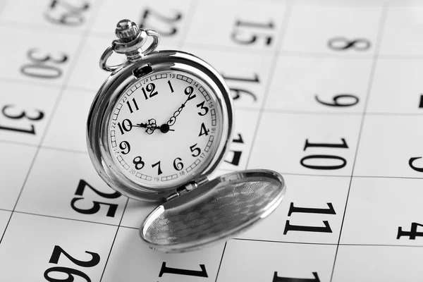 Vintage silver pocket watch laying on calender page with dates, close up — Stock Photo, Image