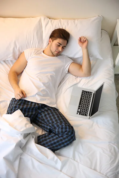 Genç adam dizüstü bilgisayarla yatakta uyuyor. — Stok fotoğraf