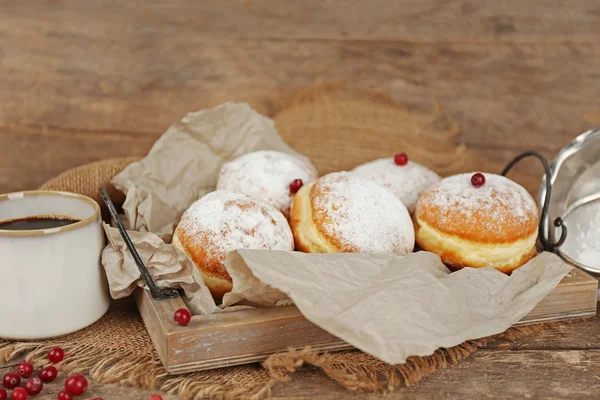 Deliciosos donuts açucarados com groselha vermelha na bandeja com pergaminho em fundo de madeira — Fotografia de Stock
