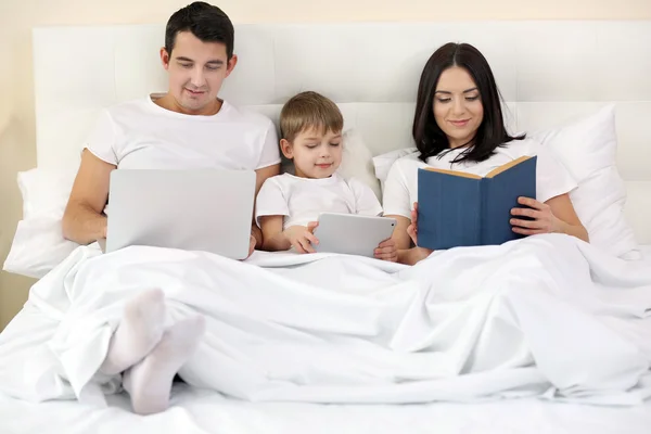 Família Descansando Com Livro Laptop Cama Casa — Fotografia de Stock