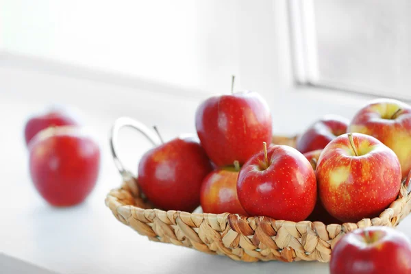 Ripe red apples in a wicker basket on windowsill — Stock Photo, Image