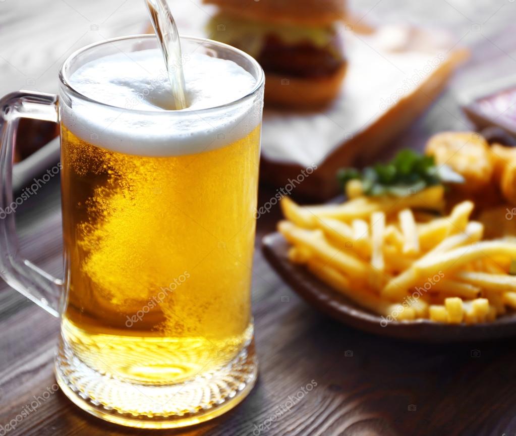 Glass mug of draft light beer with French fries on dark wooden table, close up
